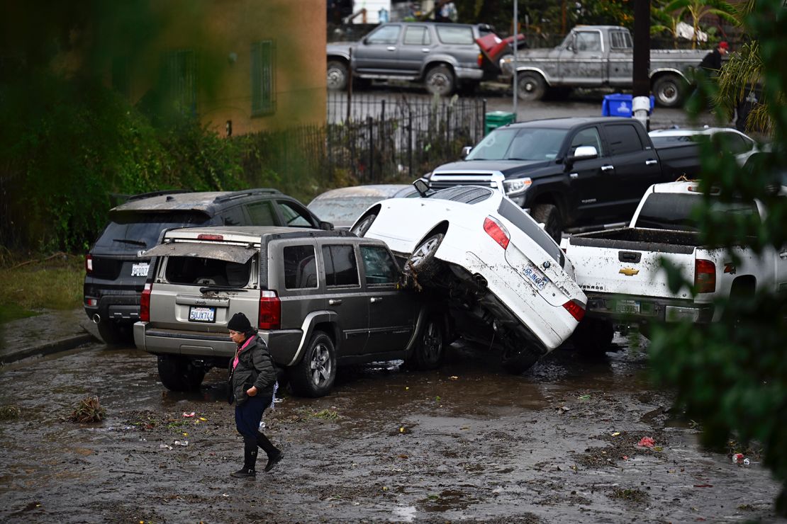A woman walks by cars damaged by floods during a rainstorm in San Diego on Monday, January 22, 2024.