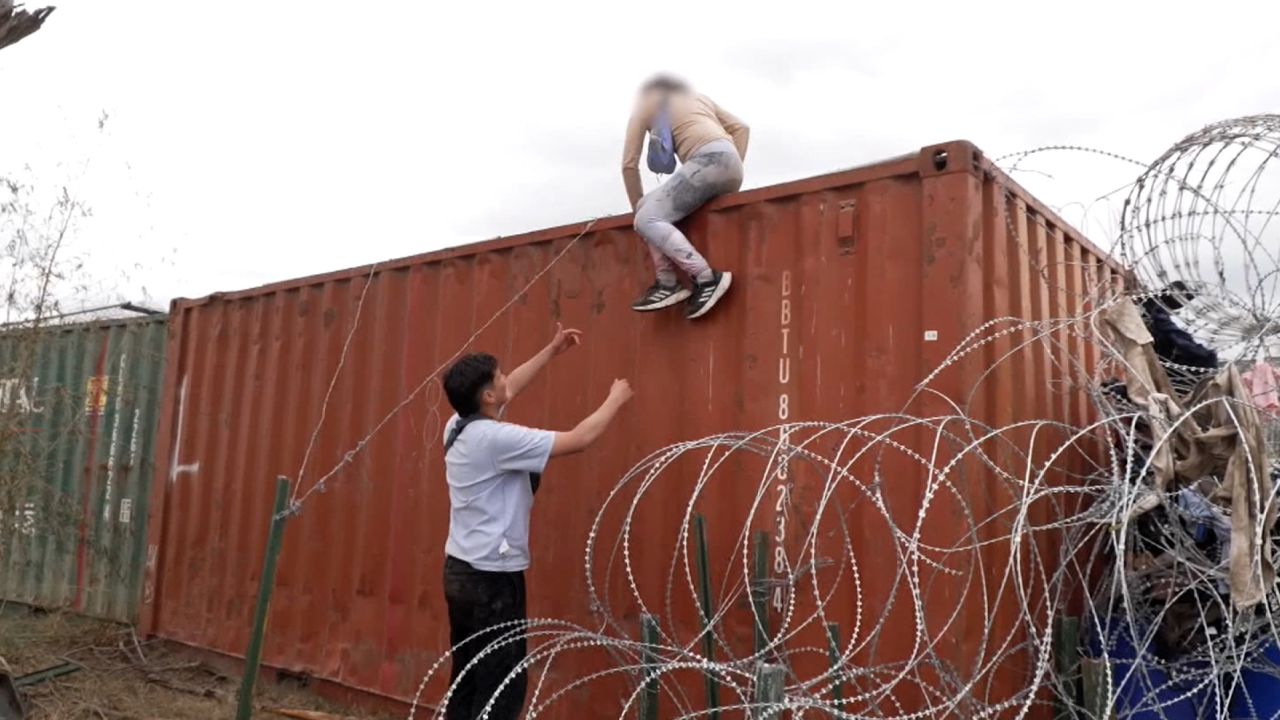 Venezuelan couple Kevin and Vanessa climb over a shipping container at the US-Mexico border. A portion of this image has been blurred by CNN to protect identity.