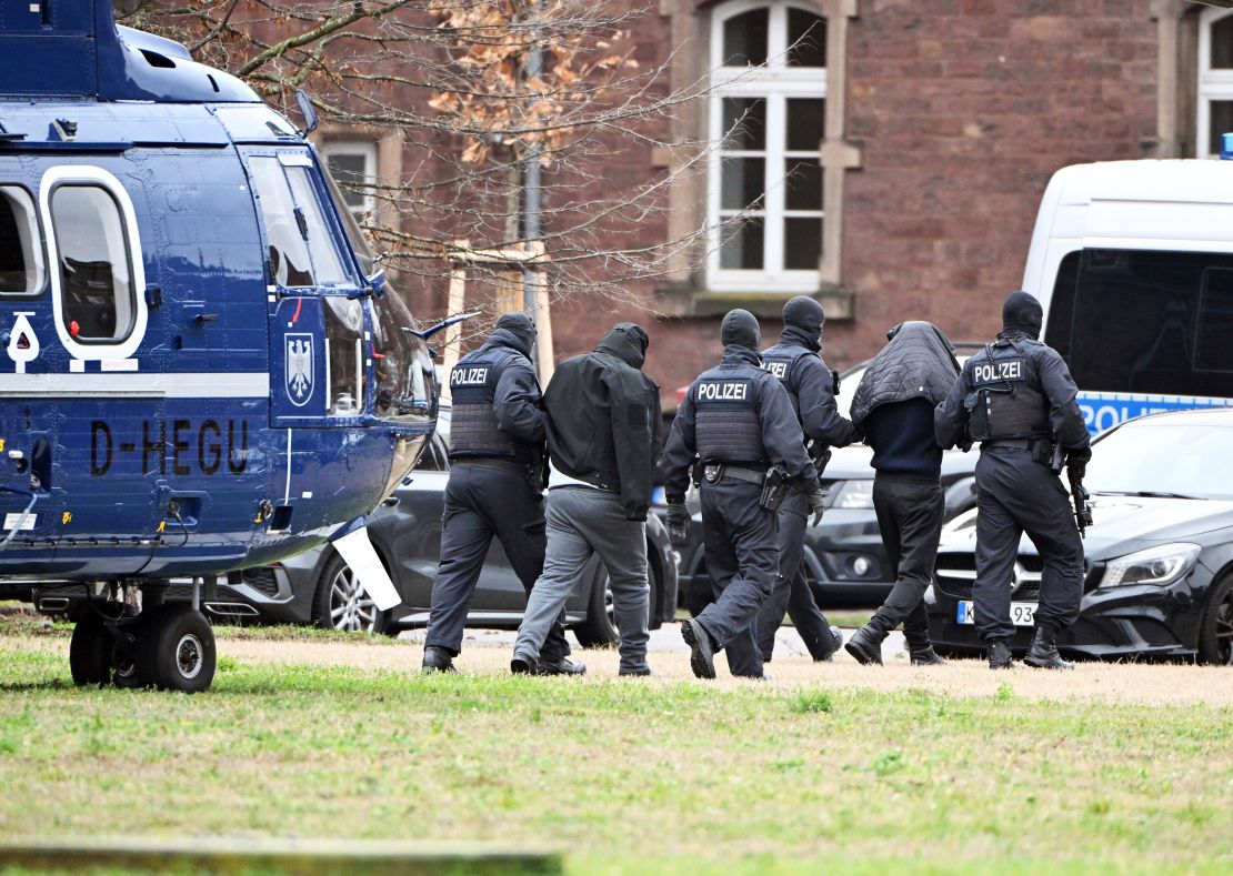 Two people are led from a helicopter to a car by police officers at a helipad in Karlsruhe, Germany, Friday Dec. 15, 2023. Denmark and Germany announced Thursday arrests of several terror suspects, including alleged Hamas members suspected of plotting attacks on Jews and Jewish institutions in Europe over the ongoing Israel-Hamas war.