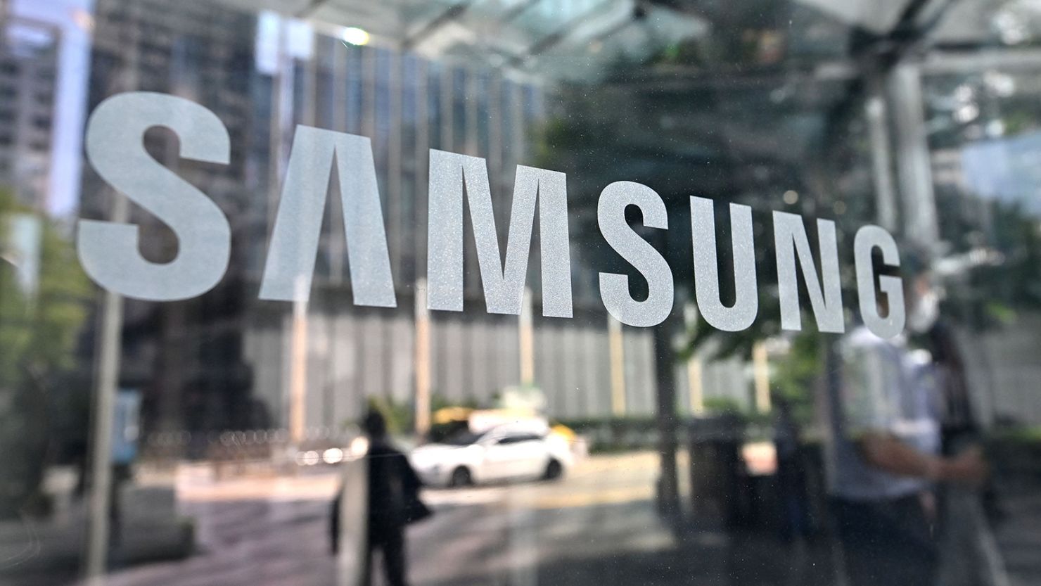 People walk past the Samsung logo displayed on a glass door at the company's Seocho building in Seoul on July 28, 2022.