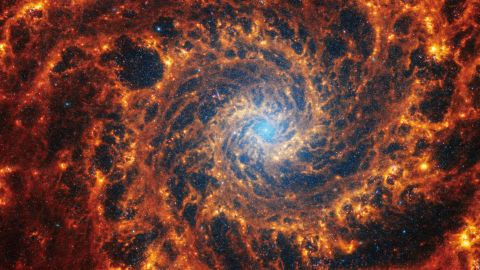 This Webb image shows a densely populated spiral galaxy anchored by a central region that has a light blue haze, known NGC 628. It's 32 million light-years away in the constellation Pisces.
