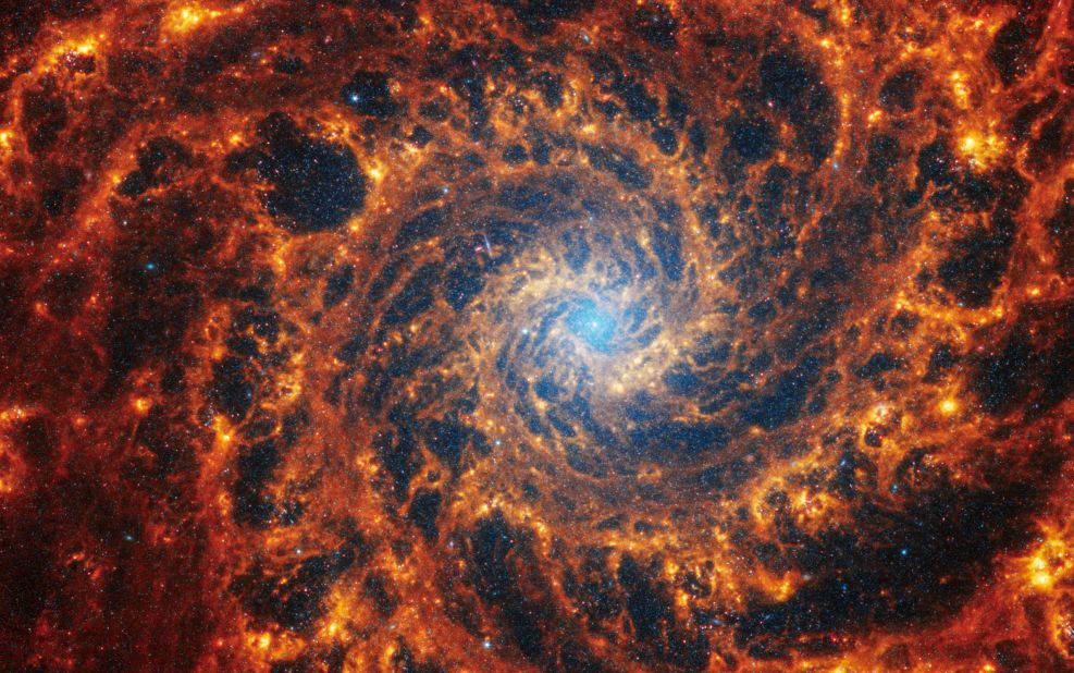 This Webb image shows a densely populated spiral galaxy anchored by a central region that has a light blue haze, known NGC 628. It's 32 million light-years away in the constellation Pisces.