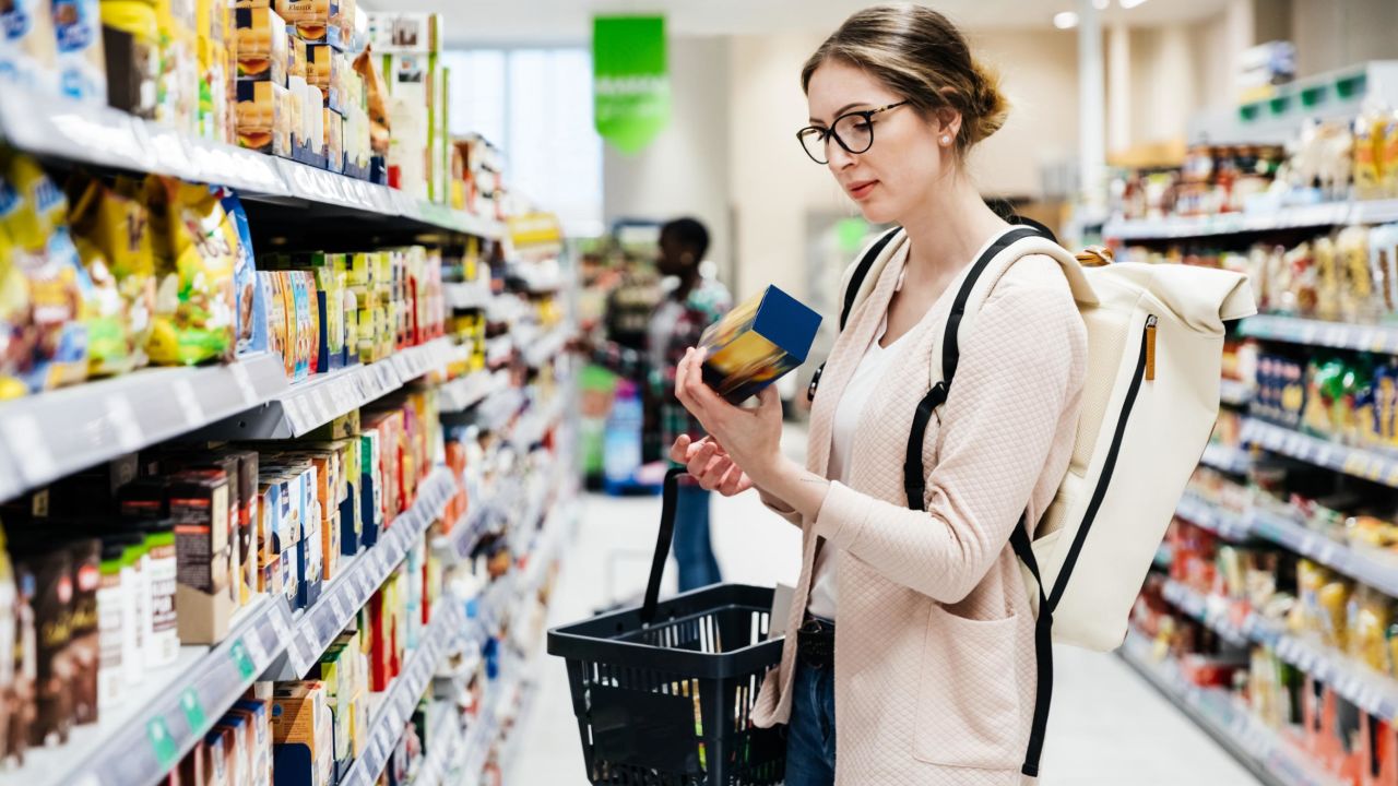 A woman reading the label on a food item while out shopping for groceries in her local supermarket.