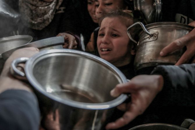 A child in Gaza joins others with empty containers as they wait to receive hot food at a charitable distribution site in Gaza City on February 26.