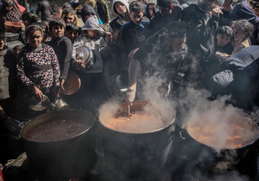 Palestinians with empty containers wait in front of boilers to receive hot food that was distributed in Gaza City on February 26.