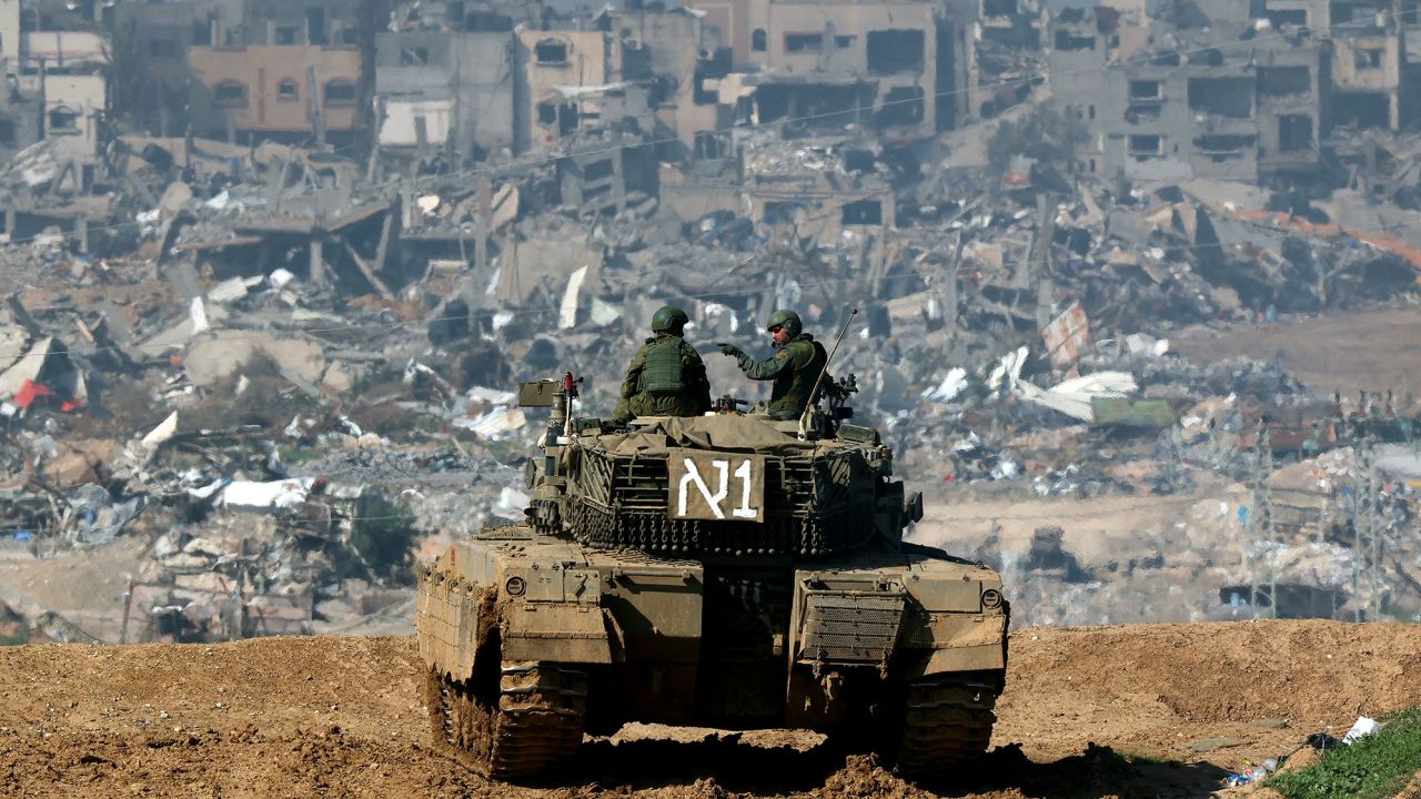 A picture taken from a position in southern Israel along the border with the Gaza Strip on January 19, 2024, shows an Israeli tank rolling along the fence as damaged buildings are see in the Gaza strip amid continuing battles between Israel and the militant group Hamas. (Photo by JACK GUEZ / AFP) (Photo by JACK GUEZ/AFP via Getty Images)