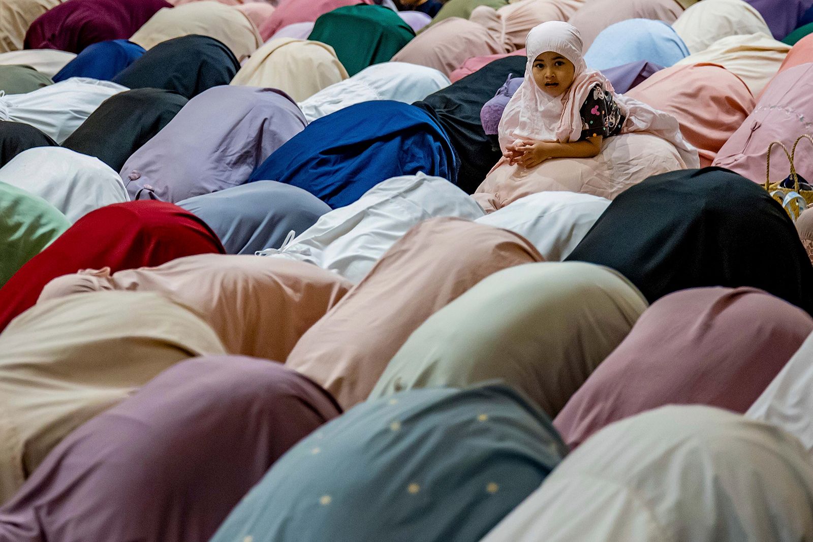 A child plays as Muslim women perform prayers on the eve of Ramadan in Seremban, Malaysia.