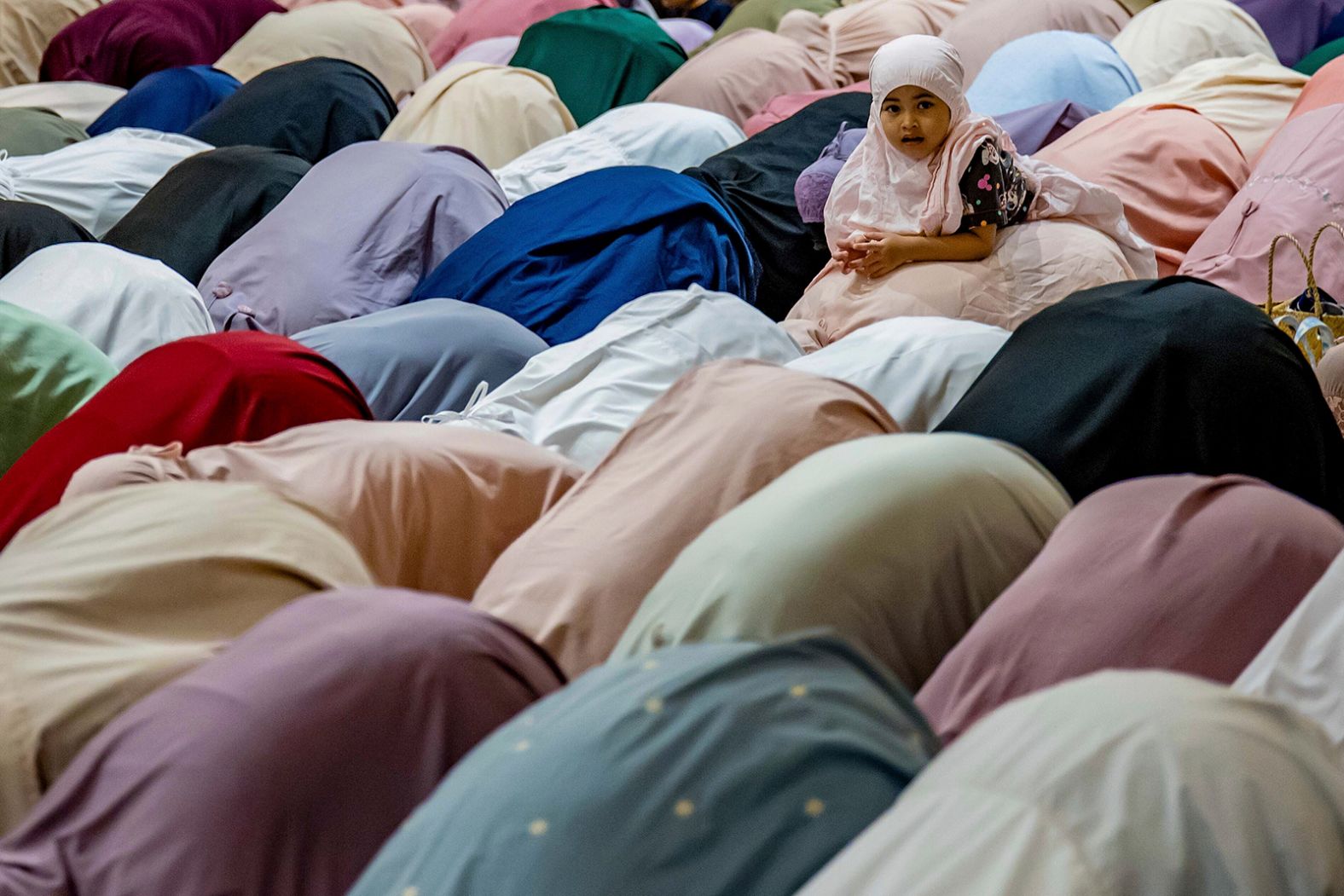 A child plays as Muslim women perform prayers on the eve of Ramadan in Seremban, Malaysia.