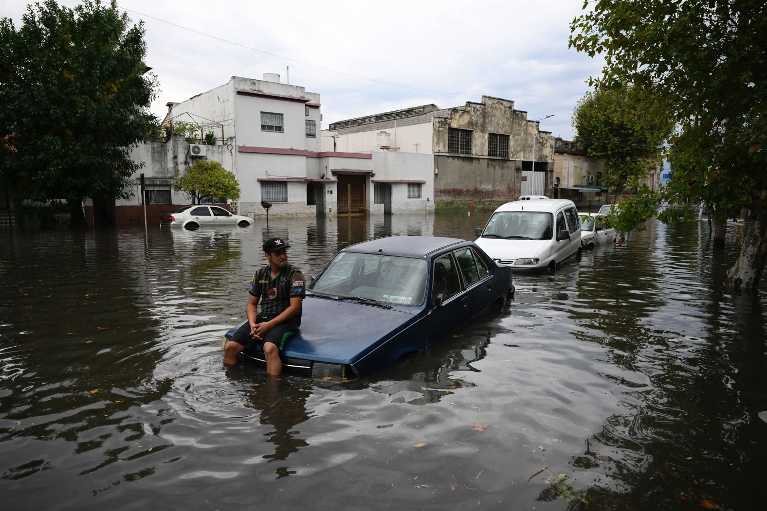 A man sits on the hood of his car in a flooded street in Avellaneda, Argentina, on Tuesday, March 12. Storms flooded parts of Buenos Aires and the area around it.