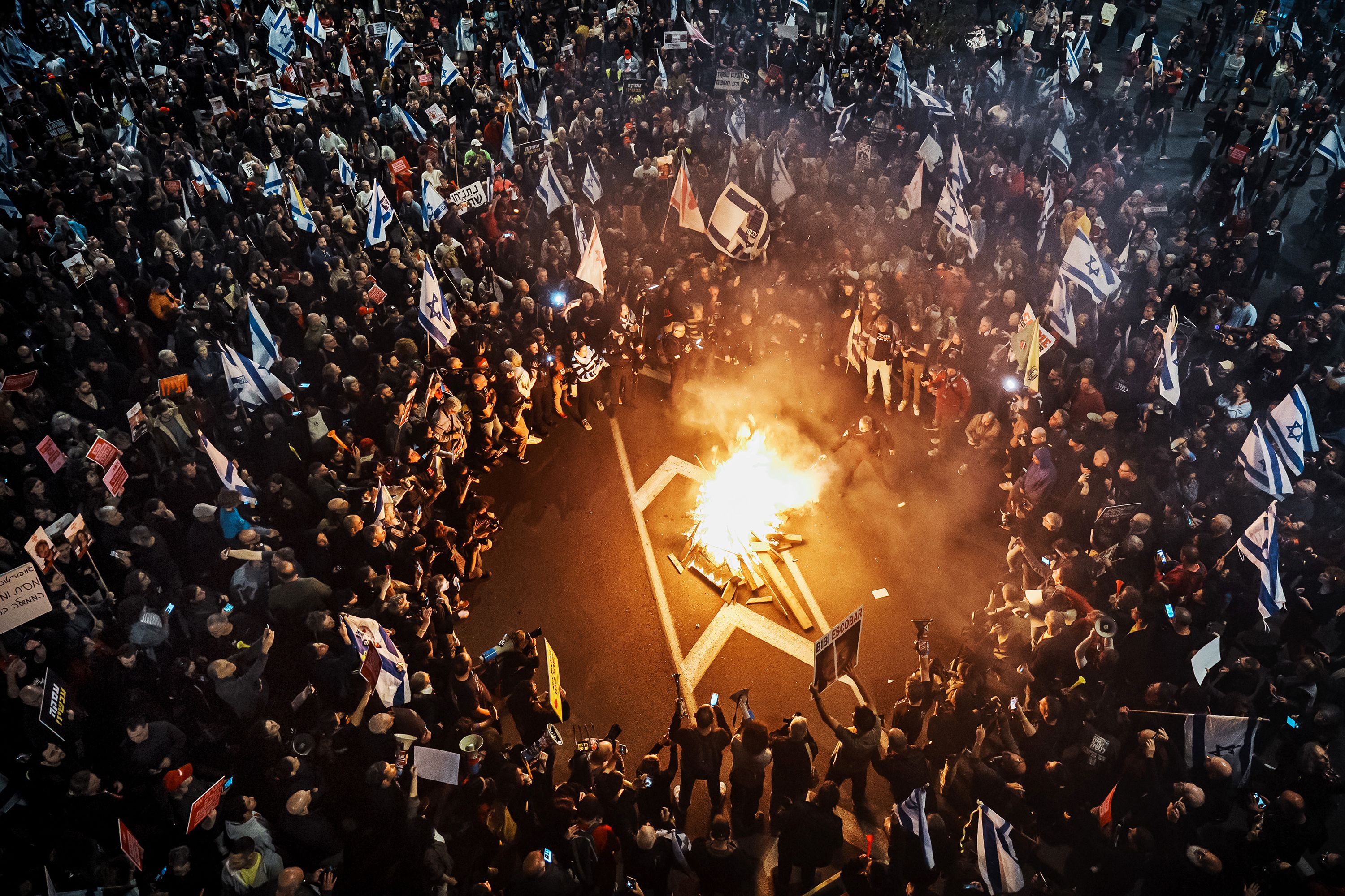 Demonstrators watch as a police officer tries to extinguish a bonfire during a protest in Tel Aviv, Israel, on Saturday, March 16.