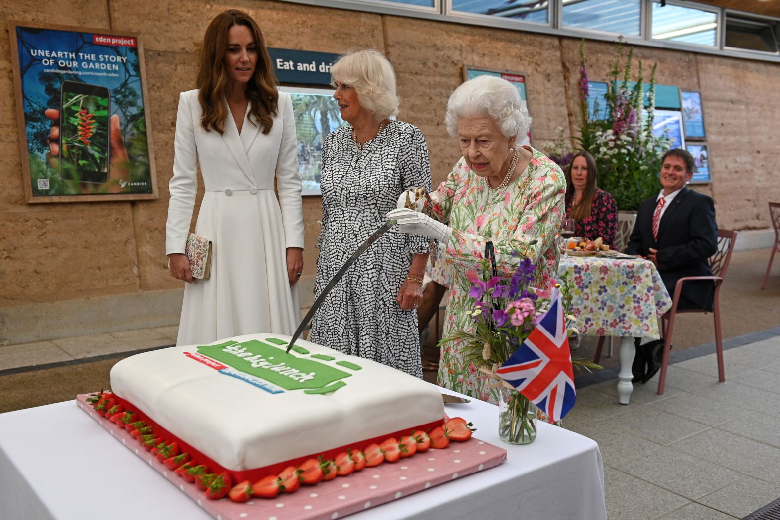 Kate and Camilla watch as Queen Elizabeth II uses a sword to cut a cake at a charity event in St. Austell, England, in 2021.