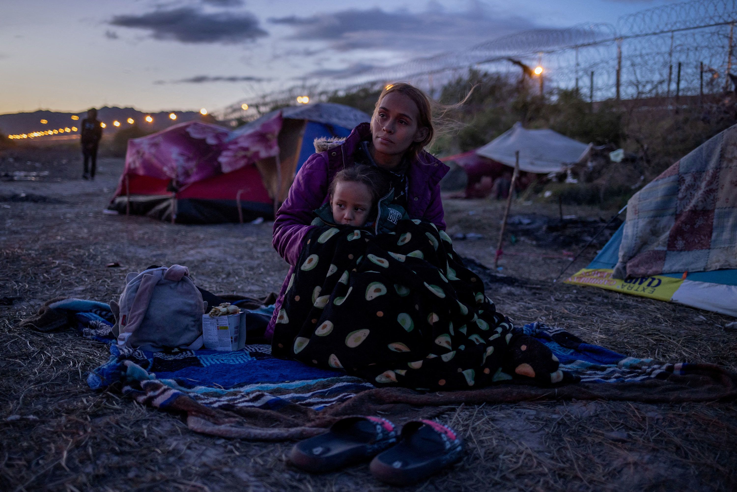 A woman stares at a fire as she covers her son with a blanket at the US-Mexico border.