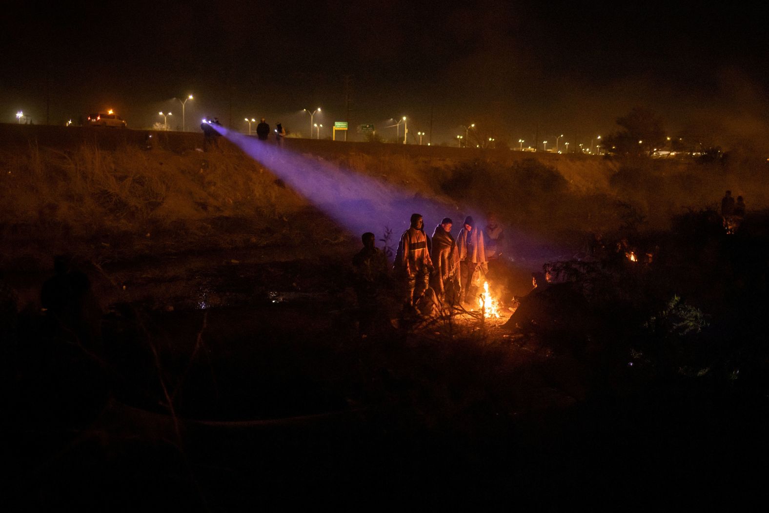 Mexican officials shine their flashlights on a group of migrants gathered around a fire at the US-Mexico border near El Paso, Texas, on Tuesday, April 2.