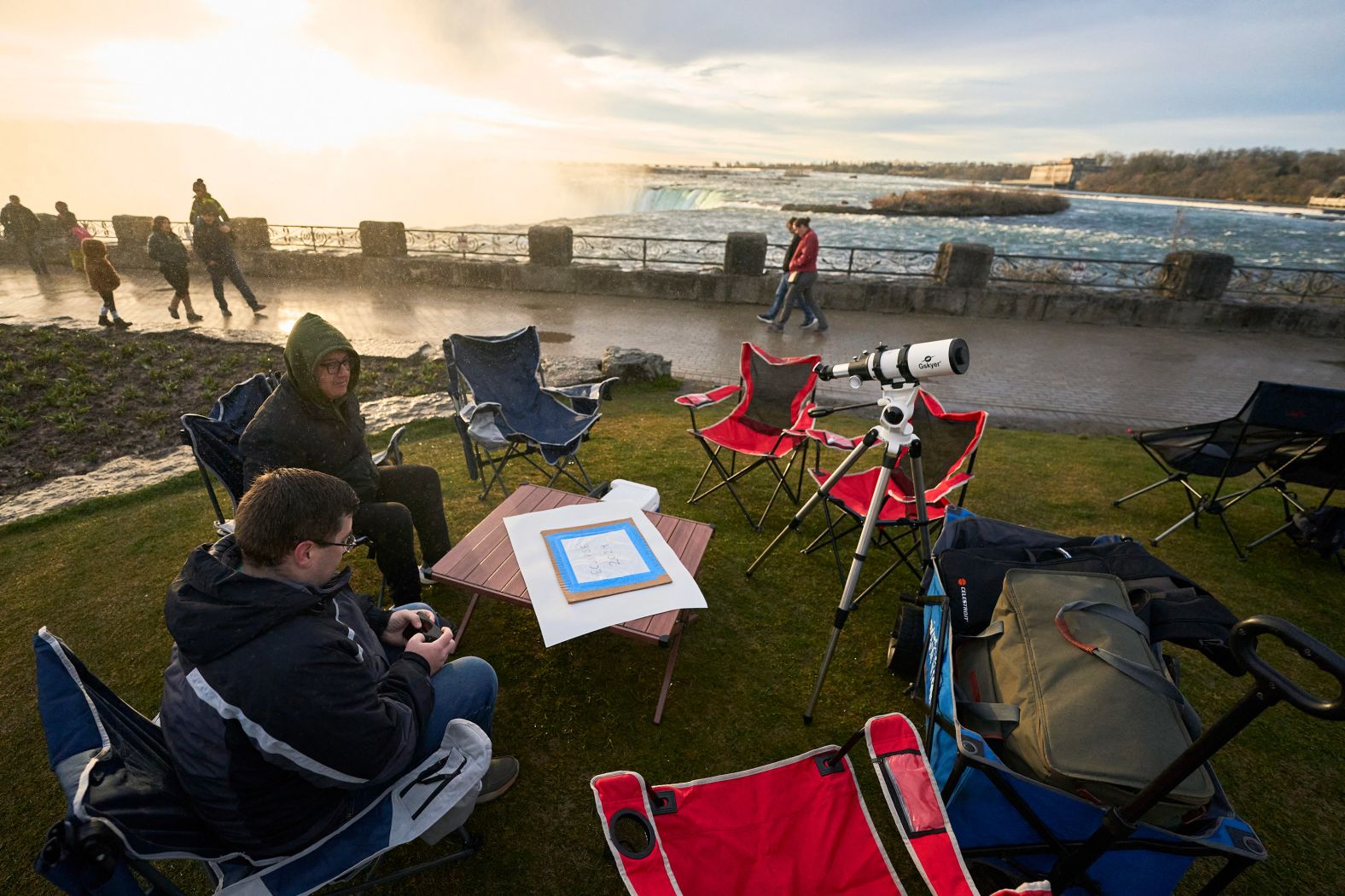 People sit next to the Horseshoe Falls in Niagara Falls as they wait for the eclipse.