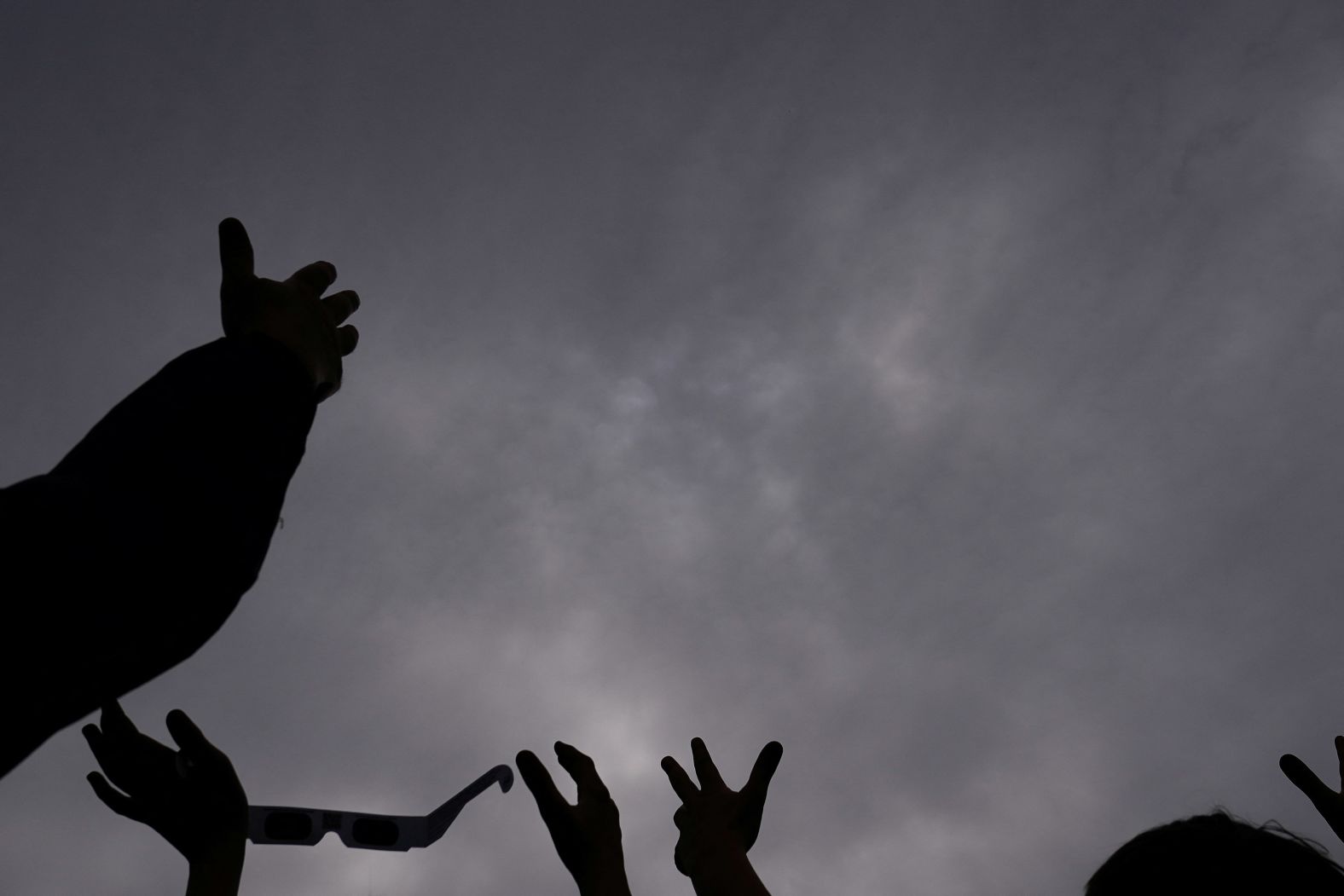 Eclipse watchers hold their hands up to the sky, hoping the clouds will part in Dunkirk, New York.