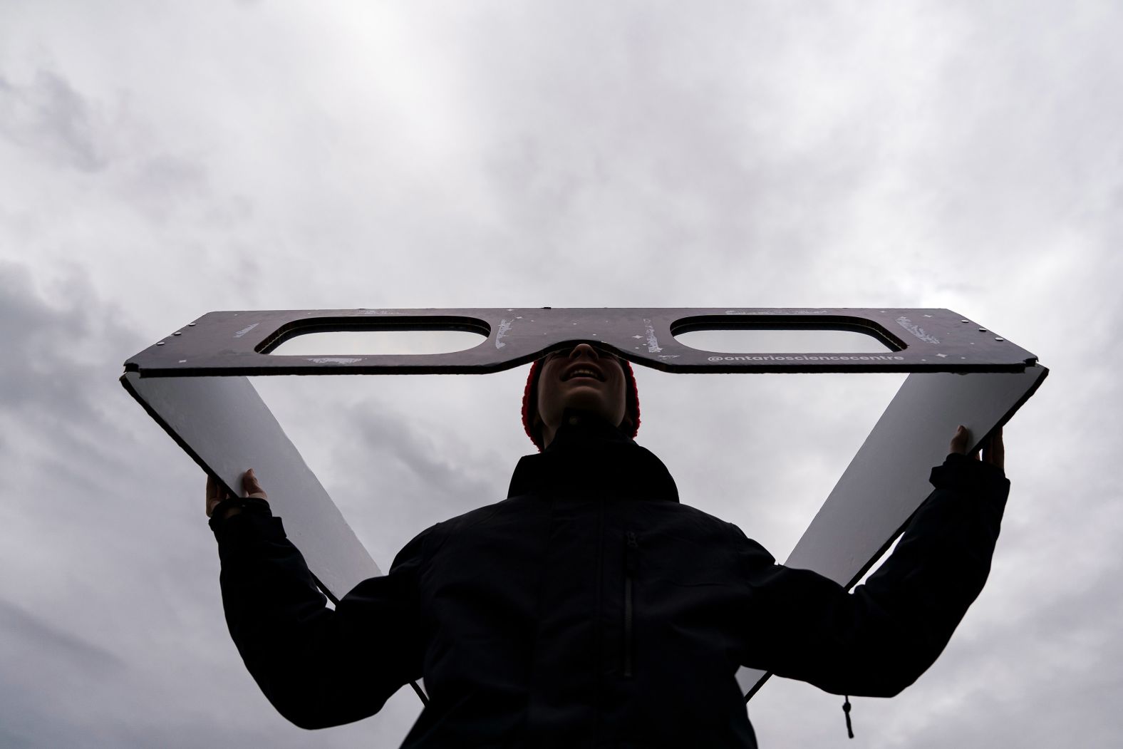 A visitor poses for a photograph with oversized eclipse glasses during a watch party at Niagara Falls in Ontario.