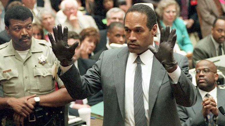 O.J. Simpson shows the jury a new pair of Aris extra-large gloves, similar to the gloves found at the Bundy and Rockingham crime scene 21 June 1995, during his double murder trial in Los Angeles,CA. Deputy Sheriff Roland Jex(L) and Prosecutor Christopher Darden (R) look on.