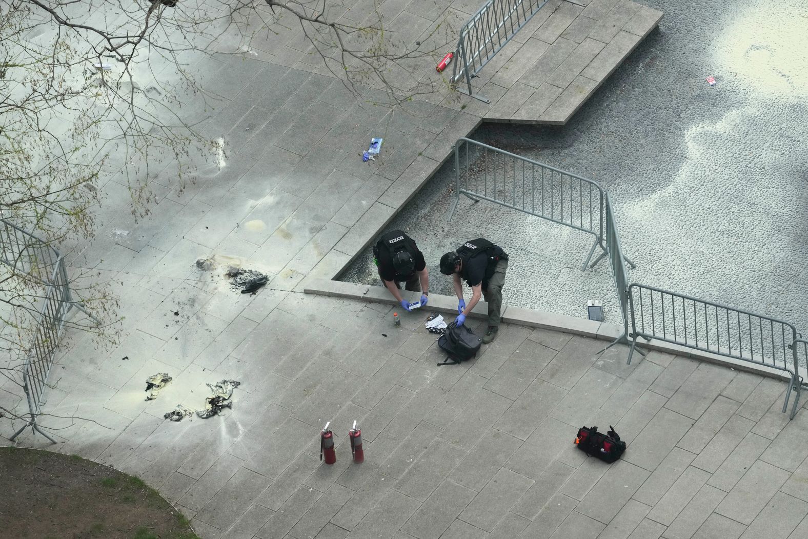 New York police officers inspect a backpack after <a href="index.php?page=&url=https%3A%2F%2Fwww.cnn.com%2Fpolitics%2Flive-news%2Ftrump-hush-money-trial-04-19-24%2Fh_a0c5ea747751ddad7bc88749d2f559d1" target="_blank">a man lit himself on fire</a> in a park outside the criminal court in Manhattan on April 19.