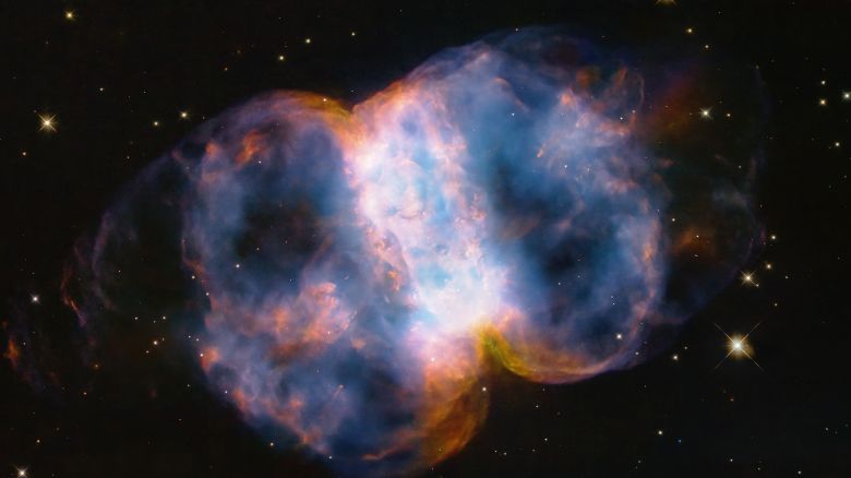 In celebration of the 34th anniversary of the launch of NASA's legendary Hubble Space Telescope, astronomers took a snapshot of the Little Dumbbell Nebula, also known as Messier 76, or M76, located 3,400 light-years away in the northern circumpolar constellation Perseus. The name 'Little Dumbbell' comes from its shape that is a two-lobed structure of colorful, mottled, glowing gases resembling a balloon that's been pinched around a middle waist. Like an inflating balloon, the lobes are expanding into space from a dying star seen as a white dot in the center. Blistering ultraviolet radiation from the super-hot star is causing the gases to glow. The red color is from nitrogen, and blue is from oxygen.