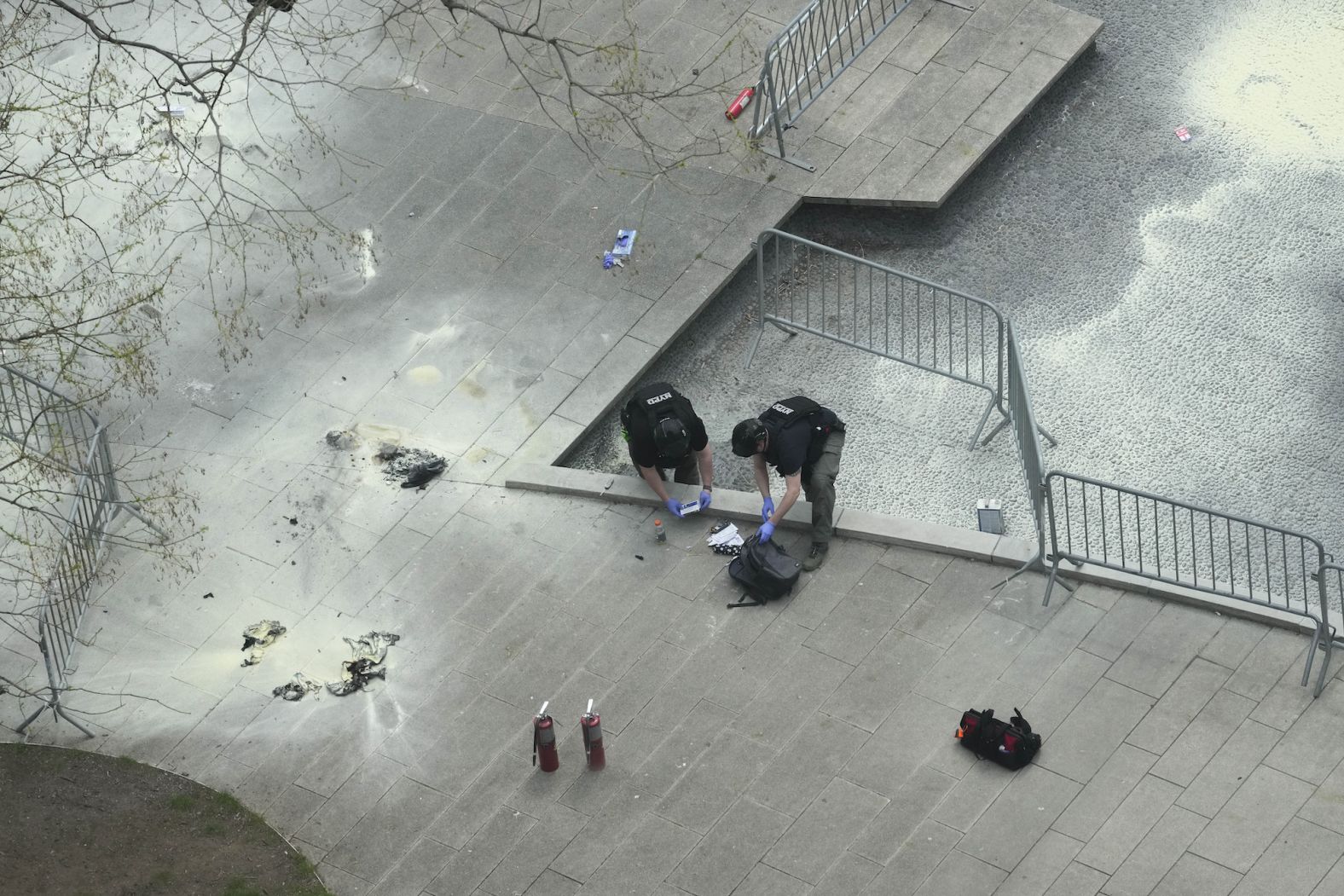New York police officers inspect a backpack on Friday, April 19, after a man <a href="index.php?page=&url=https%3A%2F%2Fwww.cnn.com%2Fpolitics%2Flive-news%2Ftrump-hush-money-trial-04-19-24%2Fh_a0c5ea747751ddad7bc88749d2f559d1" target="_blank">lit himself on fire</a> in a park outside the criminal court in Manhattan where former US President Donald Trump is standing trial.