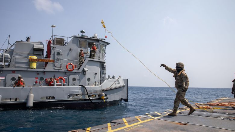 A U.S. Army Soldier tosses a line to an Army tug vessel from the Roll-On, Roll-Off Distribution Facility, or floating pier, off the shore of Gaza on May 1, 2024. The temporary pier will assist the United States Agency for International Development in the delivery of humanitarian aid to the people of Gaza.