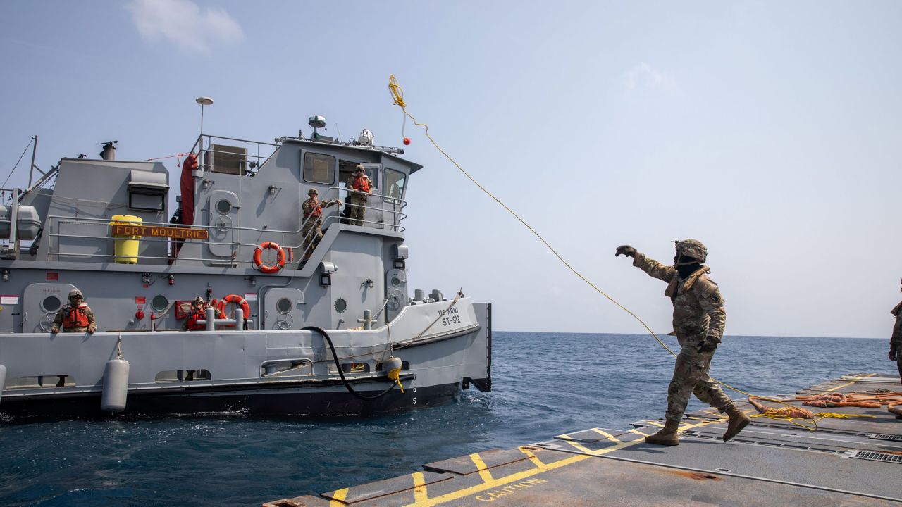 A U.S. Army Soldier tosses a line to an Army tug vessel from the Roll-On, Roll-Off Distribution Facility, or floating pier, off the shore of Gaza on May 1, 2024. The temporary pier will assist the United States Agency for International Development in the delivery of humanitarian aid to the people of Gaza.