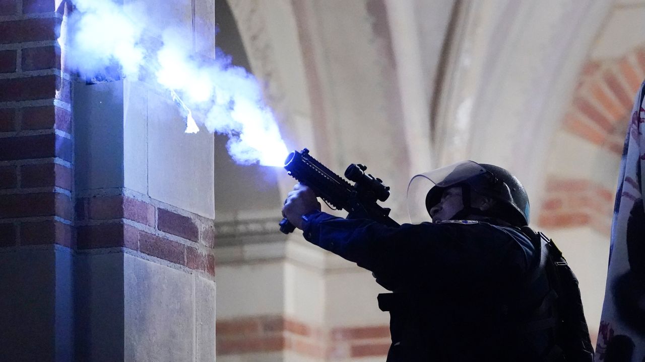 A police officer launches a smoke bomb on the UCLA campus during a raid on a pro-Palestinian encampment Thursday, May 2, 2024, in Los Angeles.