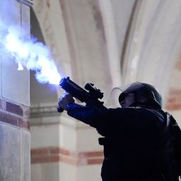 A police officer launches a smoke bomb on the UCLA campus during a raid on a pro-Palestinian encampment Thursday, May 2, 2024, in Los Angeles.