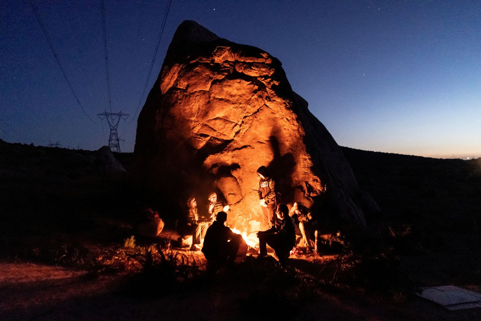 Asylum-seeking migrants from India and Colombia sit around a fire to keep warm on Saturday, April 27, after crossing the US-Mexico border in <a href="index.php?page=&url=https%3A%2F%2Fwww.cnn.com%2Finteractive%2F2024%2F02%2Fworld%2Fmigrant-crossing-california-cnnphotos%2F" target="_blank">Jacumba Hot Springs</a>, California.