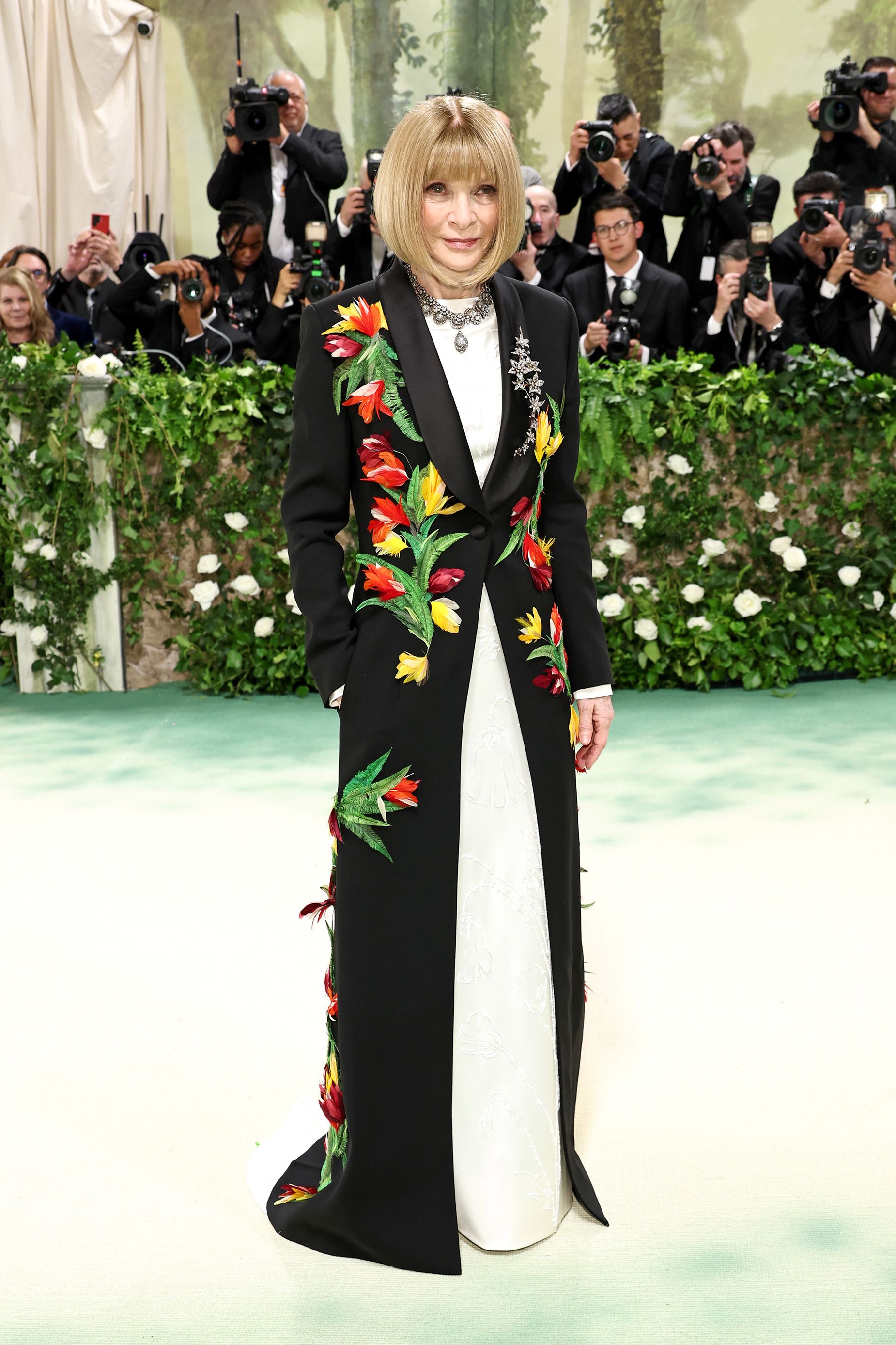 American Vogue editor Anna Wintour in a custom floral Loewe look inspired by a 1944 evening cape by designer Charles James. Tailored in wool with a silk satin shawl collar, the tuxedo is decorated with floral motifs using hand-dyed feathers, tonal beading and pearl embroidery. 