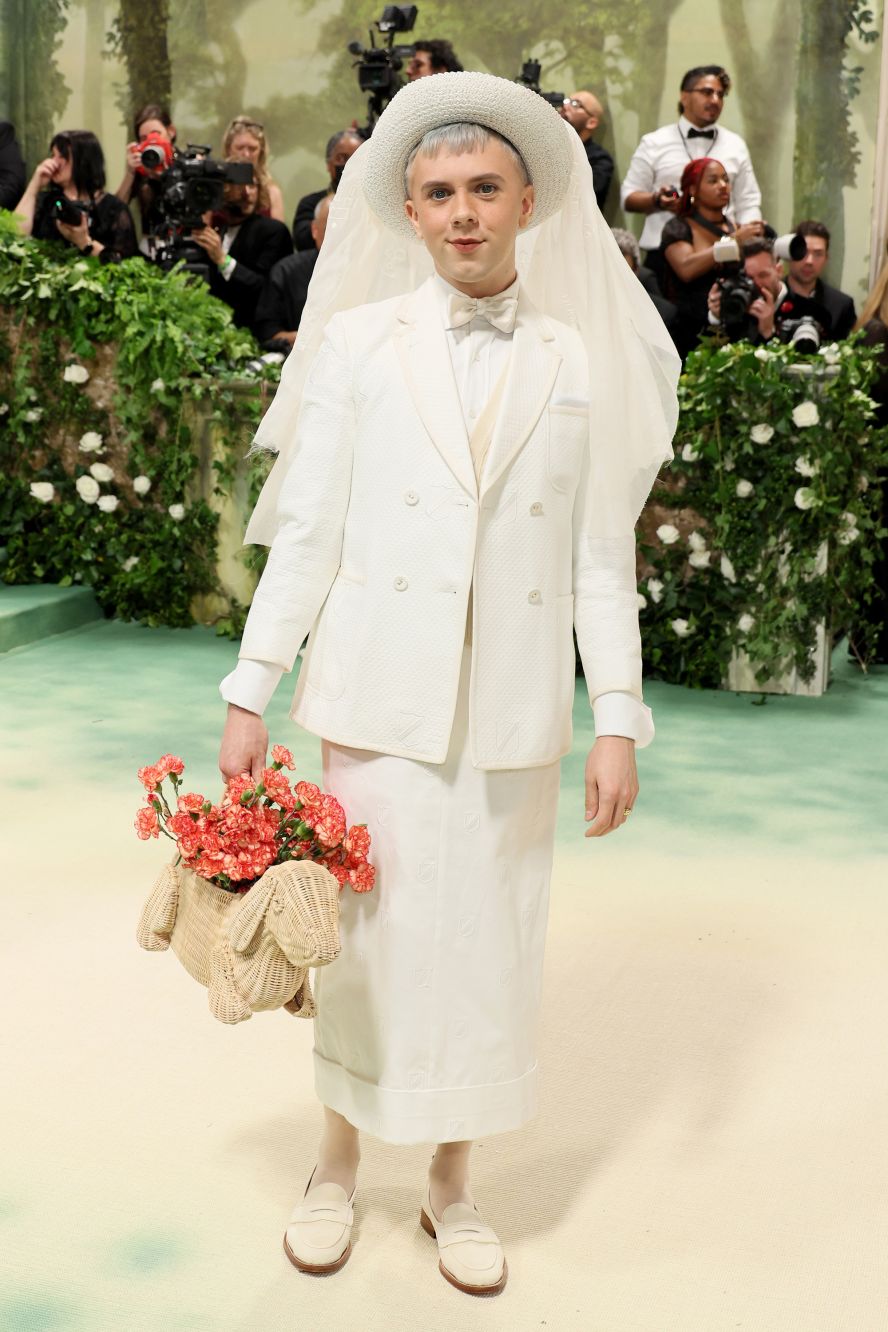 Cole Escola in a bridal-looking all-white ensemble and wicker dog purse filled with carnations. 