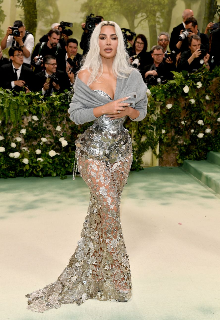 Kim Kardashian was in custom Maison Margiela, with a metal bodice and a silver floral overlay. She wore a gray, pilling cardigan over her shoulders. 
