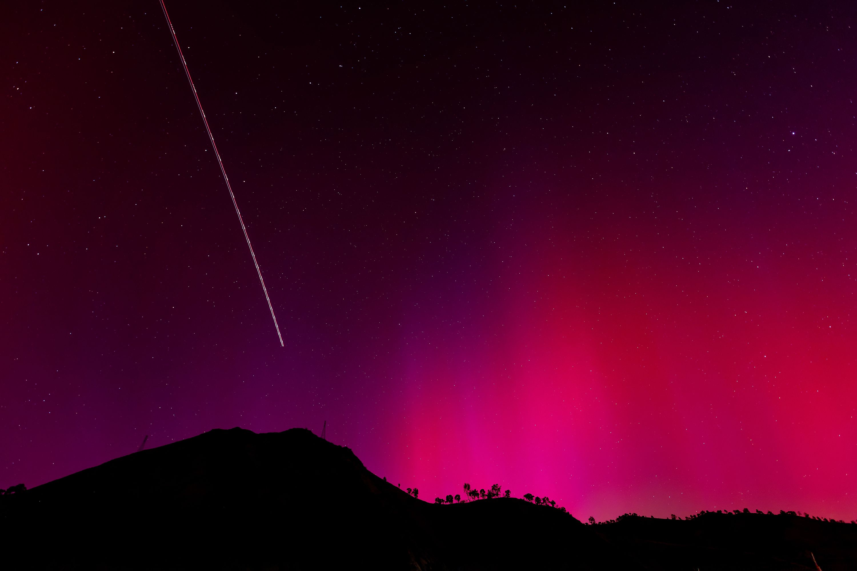 In this long exposure photo، the blinking lights of a plane streak through the aurora borealis over Lake Berryessa، California، on May 11.