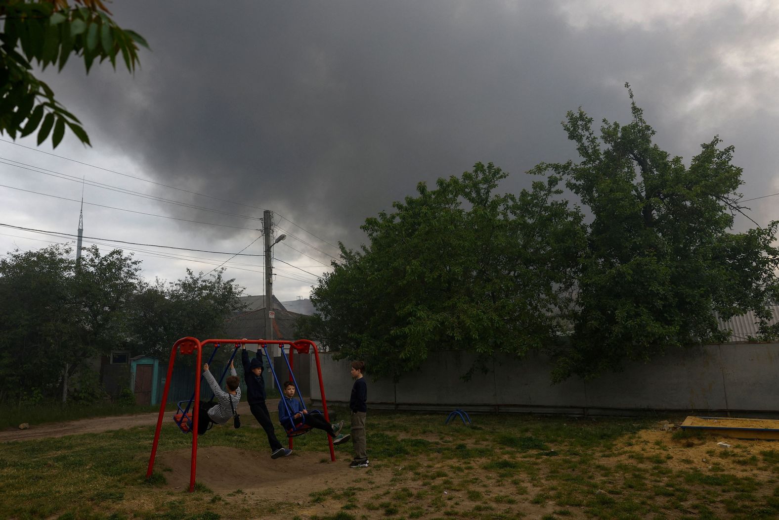 Boys play on a playground in Kharkiv, Ukraine, as smoke rises from a nearby Russian missile strike on Friday, May 17.