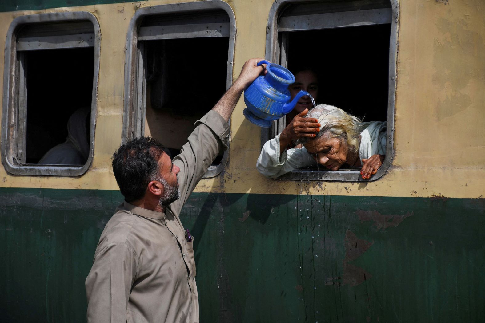A woman, leaning out of a train window, receives water on her head to cool off during a hot and humid day in Hyderabad, Pakistan, on Wednesday, May 22.