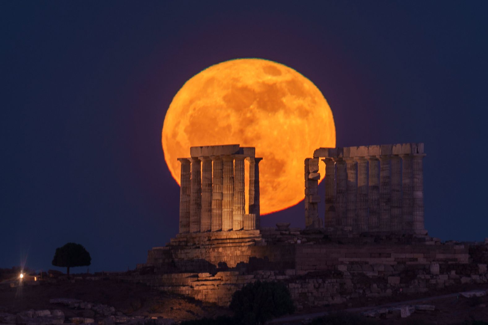A full moon rises behind the Temple of Poseidon at Cape Sounion, about 70 kilometers (45 miles) south of Athens, Greece, on Thursday, May 23.