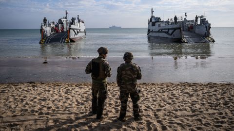 TOPSHOT - French troops of the 3rd fusilier marin regiment stand on the beachfron looking at the French navy amphibious helicopter carrier Mistral (far, rear) and landing crafts (front) during a joint US and French amphibious landing operation showcase, on June 4, 2024, at Omaha beach in Saint-Laurent-sur-Mer, northwestern France, ahead of the "D-Day" commemorations marking the 80th anniversary of the World War II Allied landings in Normandy. (Photo by LOIC VENANCE / AFP) (Photo by LOIC VENANCE/AFP via Getty Images)