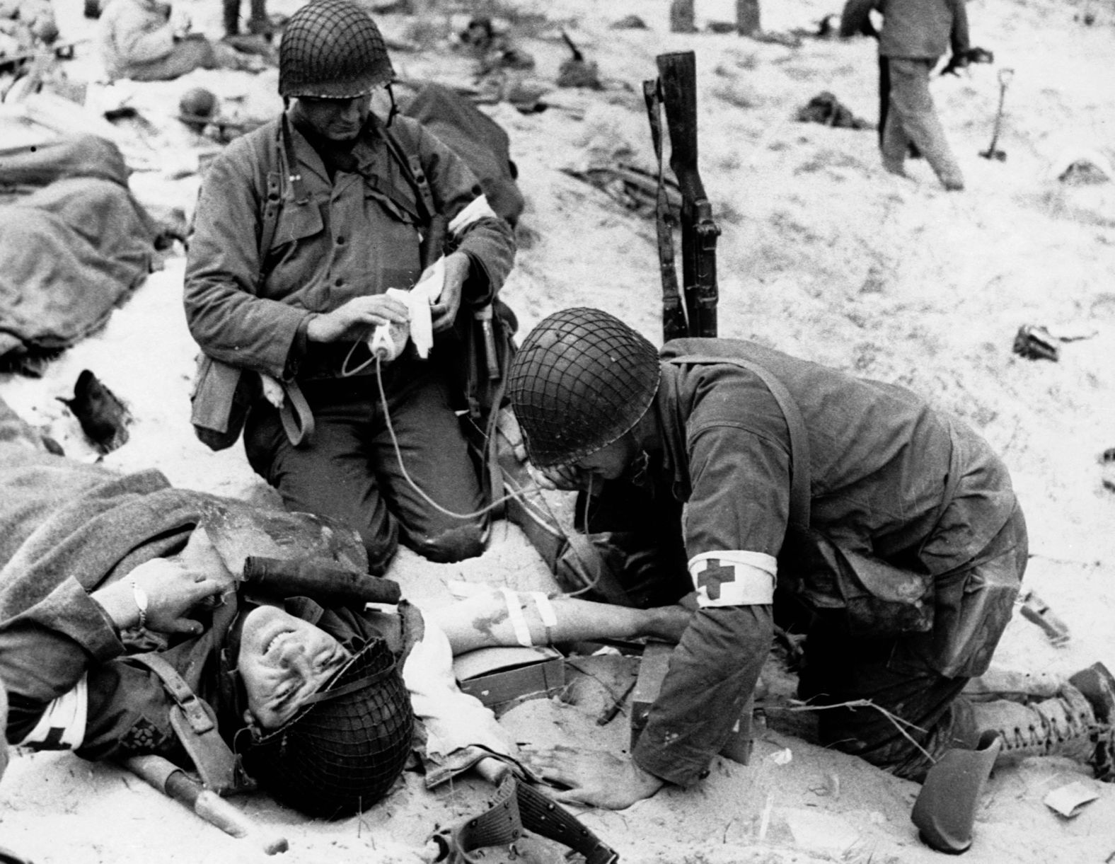 Medics start an IV as they assist a wounded soldier on shore. Heavy fire from German positions caused many casualties.