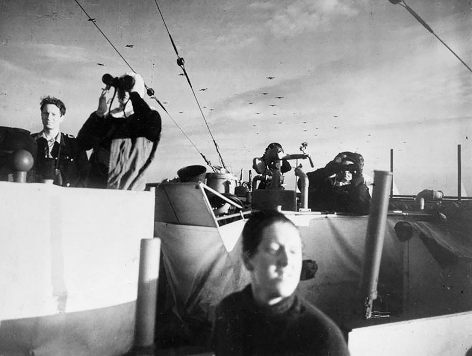 The crew on the British frigate HMS Holmes keep watch as gliders pass overhead with reinforcements from the 6th Airborne Division.