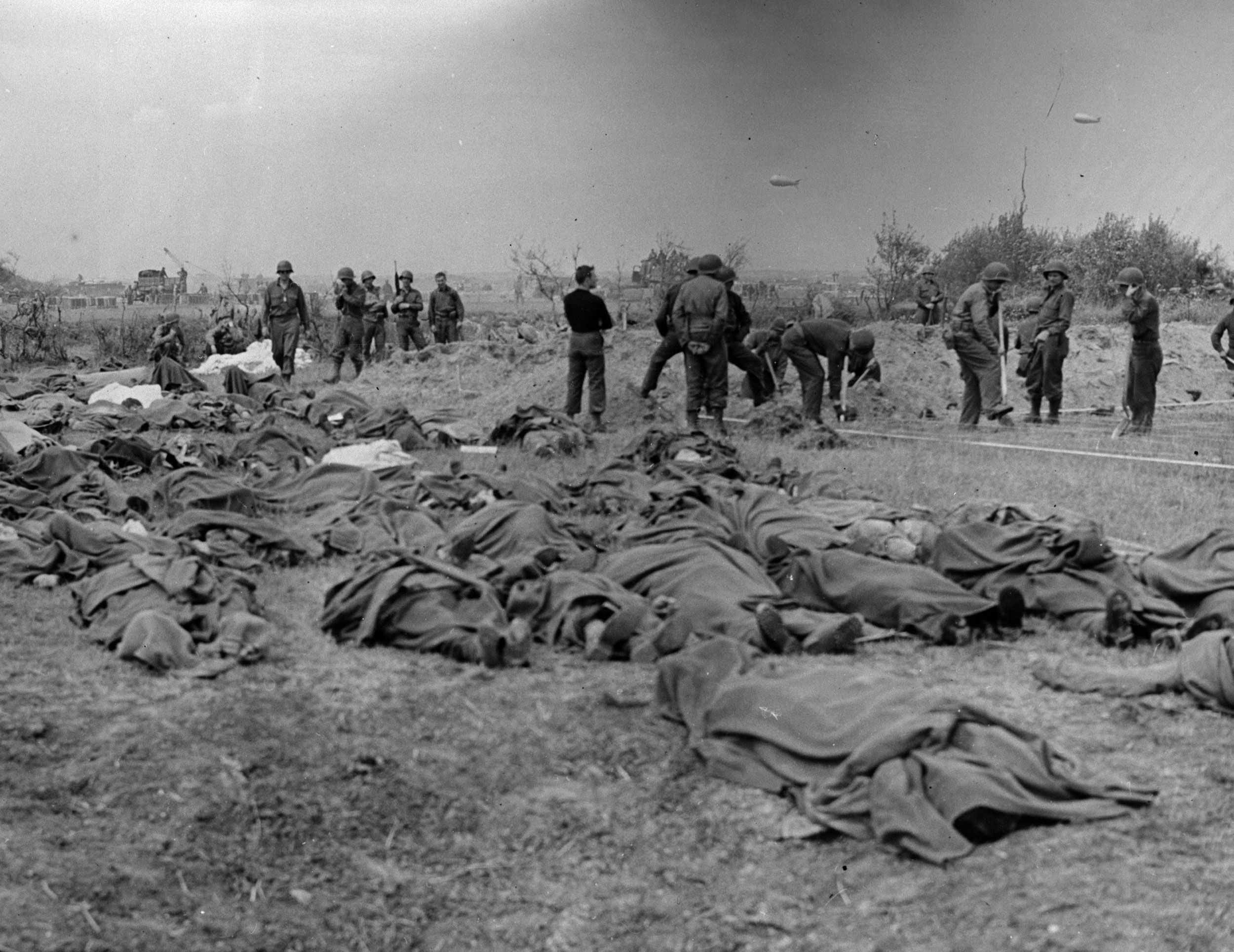 Bodies of American soldiers lie on the ground in Normandy as graves are dug.