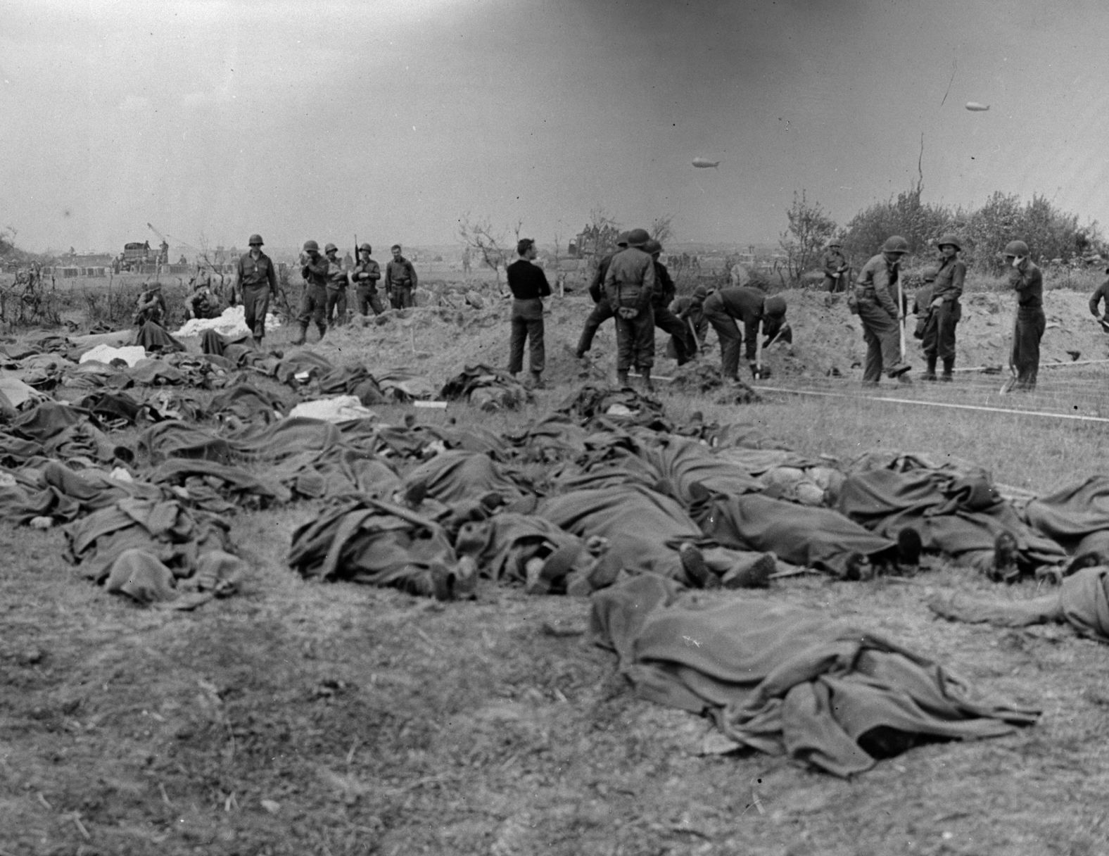 Bodies of American soldiers lie on the ground in Normandy as graves are dug.