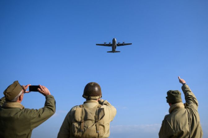 Enthusiasts dressed in replica attire react as a Lockheed C-130 Hercules flies over Utah Beach on Thursday.