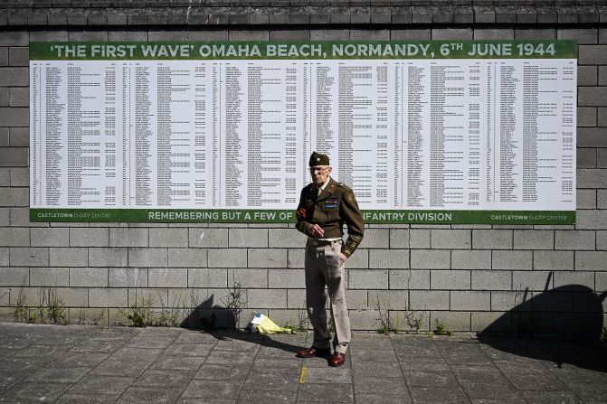 A man wearing a World War II-era uniform stands in front of a board at the D-Day Centre in Portland, England, on Thursday. The board displays names of D-Day soldiers who left in the first wave from Portland 80 years ago.