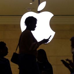 FILE PHOTO: A women uses an iPhone mobile device as she passes a lighted Apple logo at the Apple store at Grand Central Terminal in New York City, U.S., April 14, 2023. REUTERS/Mike Segar/File Photo