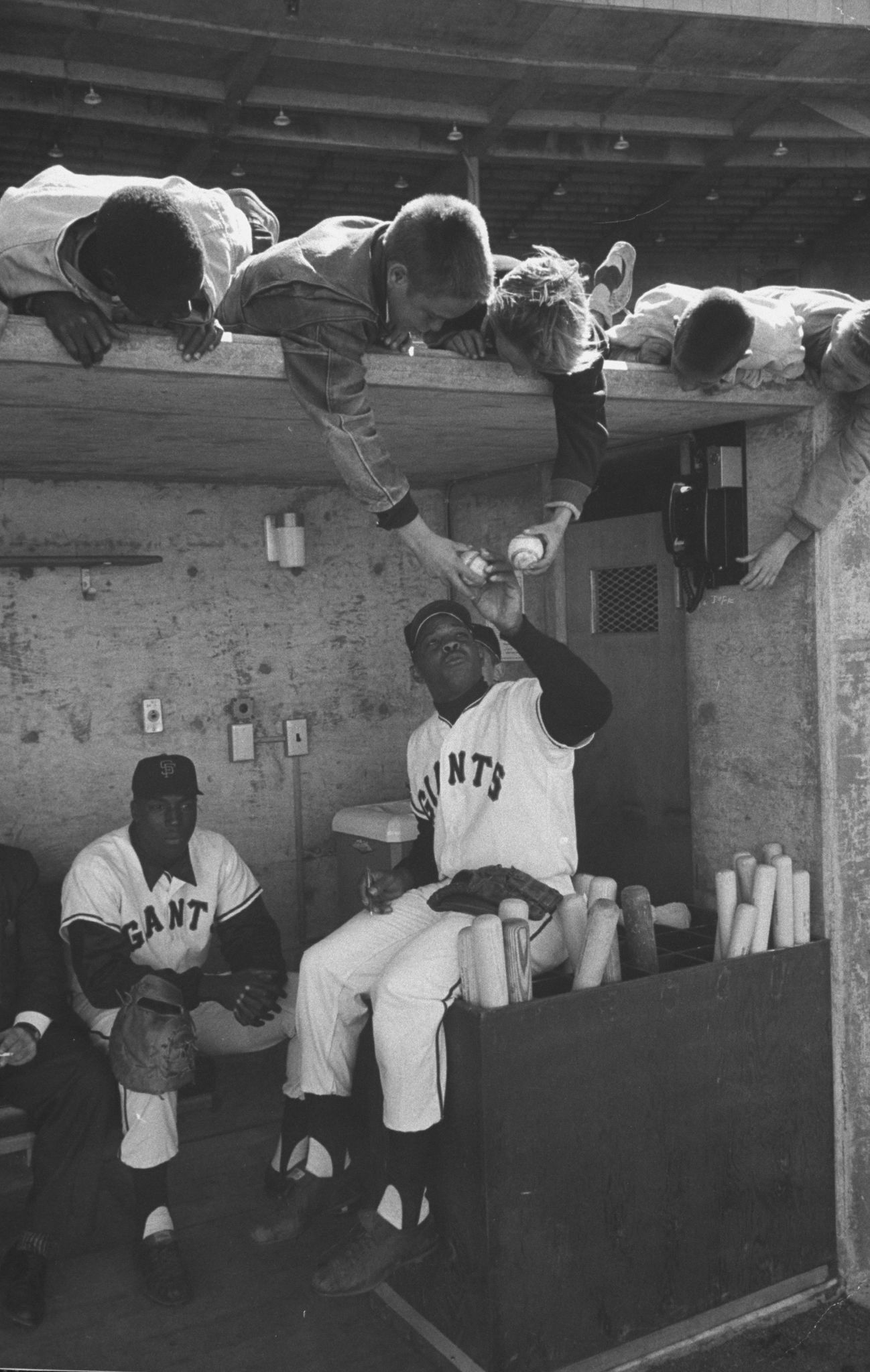 Mays interacts with young fans while sitting with Willie McCovey in the dugout of Candlestick Park in 1960.