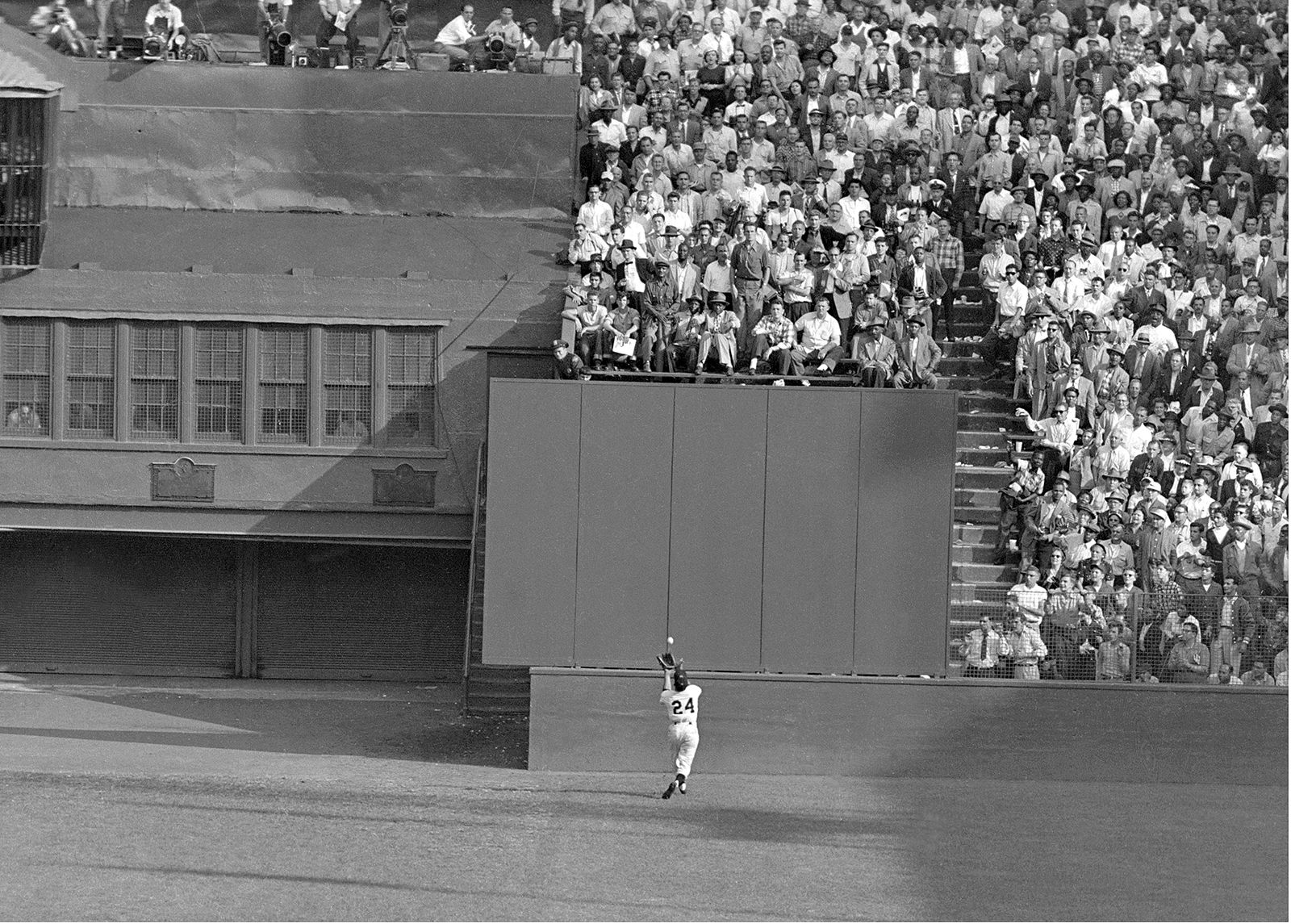 Sprinting toward the center-field wall, his back fully turned to the plate, Mays catches a ball over his shoulder during the first game of the 1954 World Series.