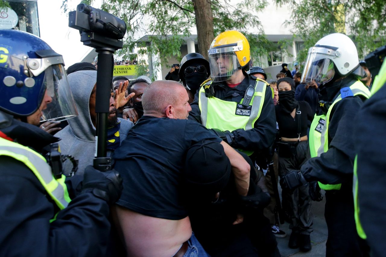 A group of men carry an injured man away after he was allegedly attacked by some of the crowd of protesters, as police try to intervene on the Southbank near Waterloo station in London on June 13, 2020.