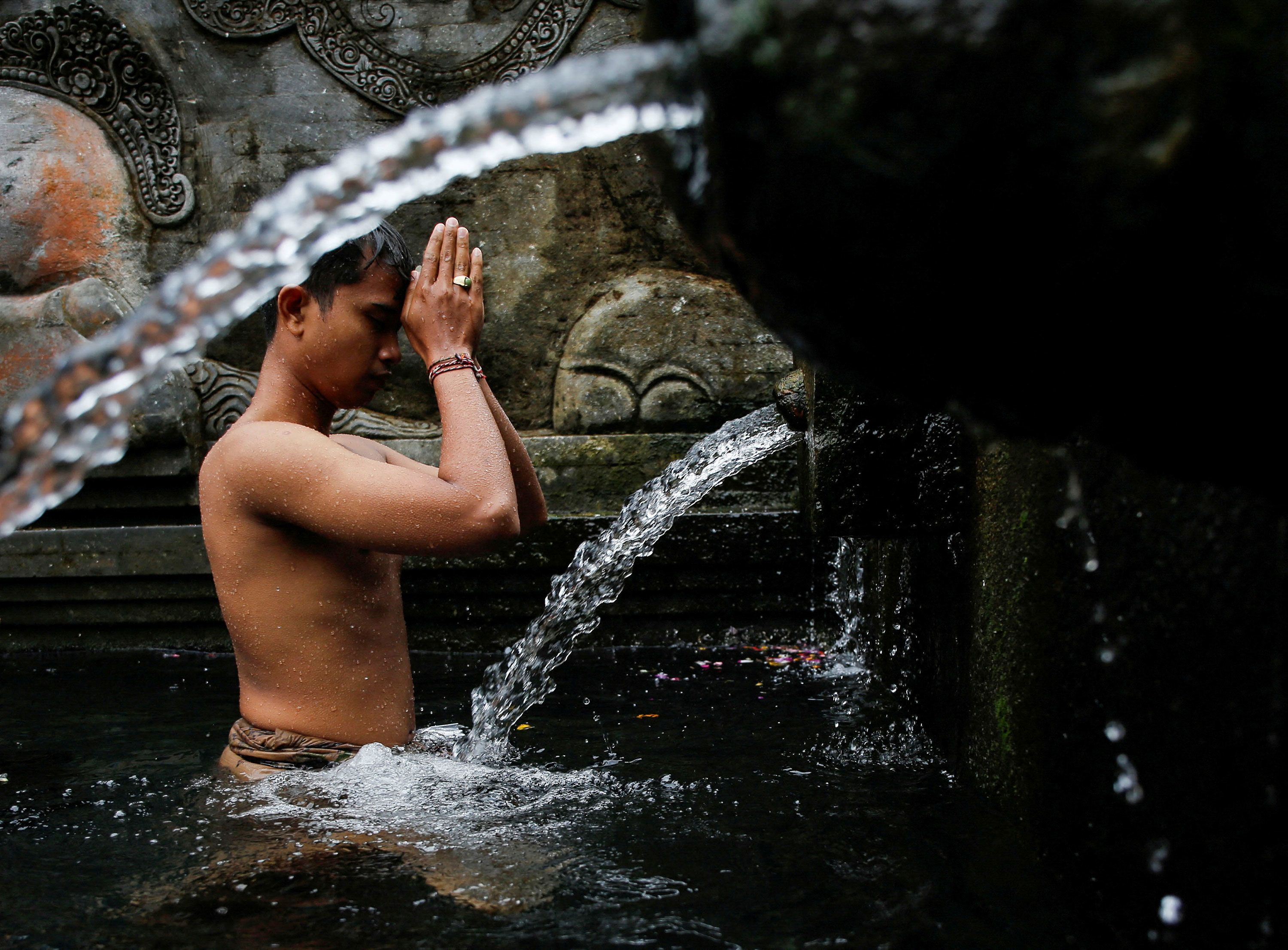 A person prays before taking a bath during a Hindu cleansing ritual called Banyu Pinaruh at the Tirta Empul temple's holy spring in Bali, Indonesia, on Sunday, July 14.