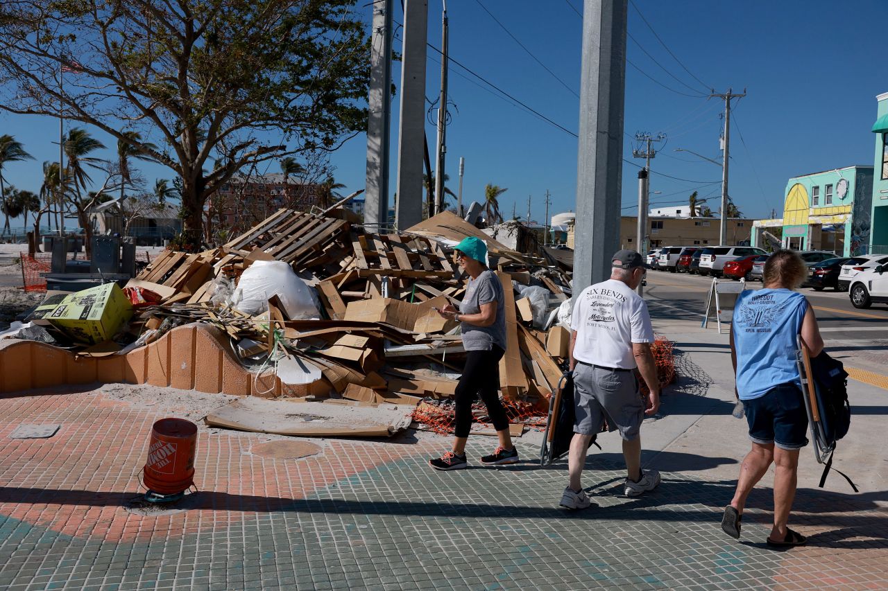 Beachgoers walk past a pile of Hurricane Ian debris on January 25, 2023, in Fort Myers Beach, Florida.