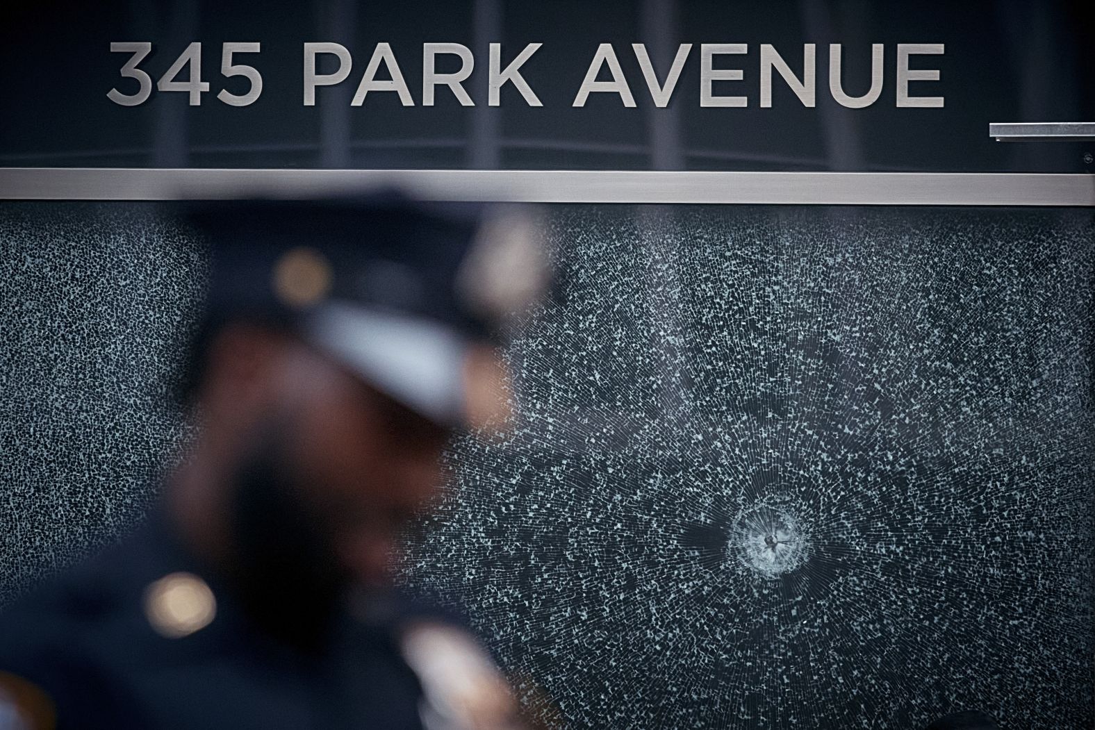 Police officers stand watch near broken glass at the entrance of the Park Avenue skyscraper where a mass shooting took place in New York on Monday, July 28.
